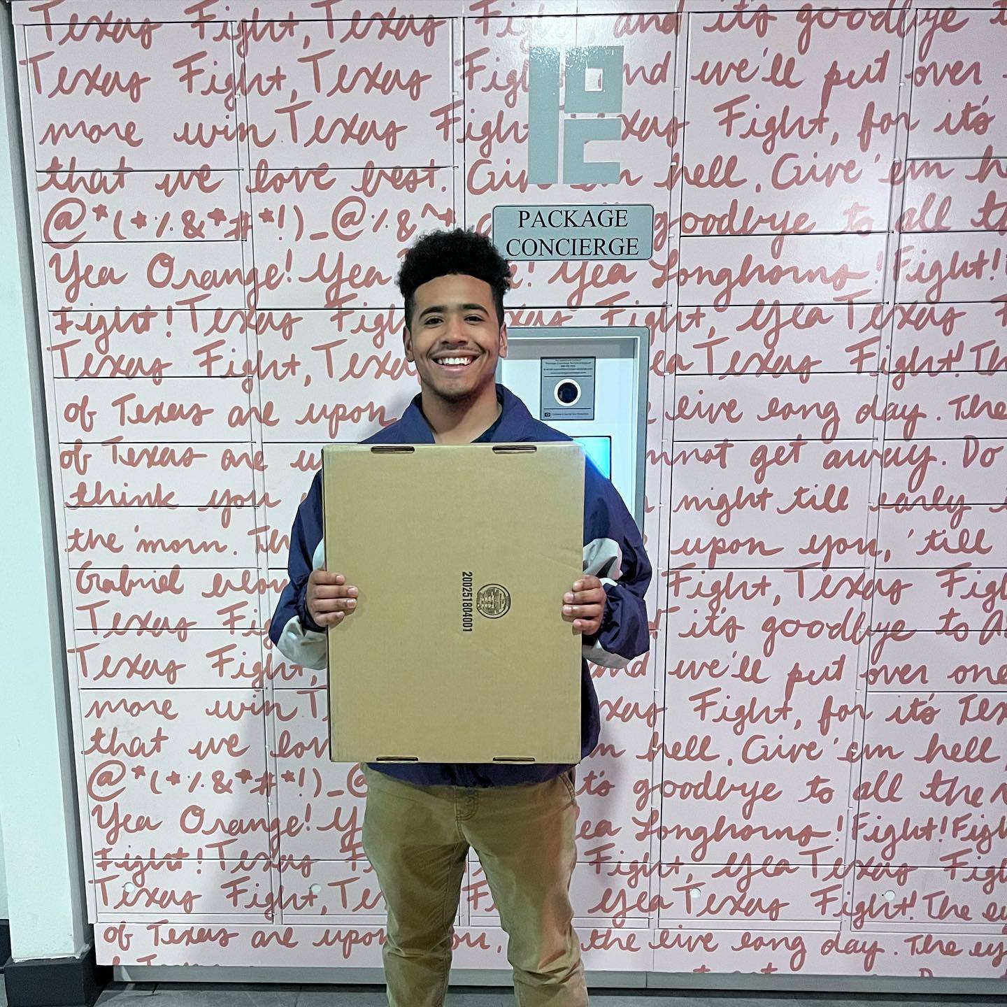 Smiling student holding package in front of smart package locker